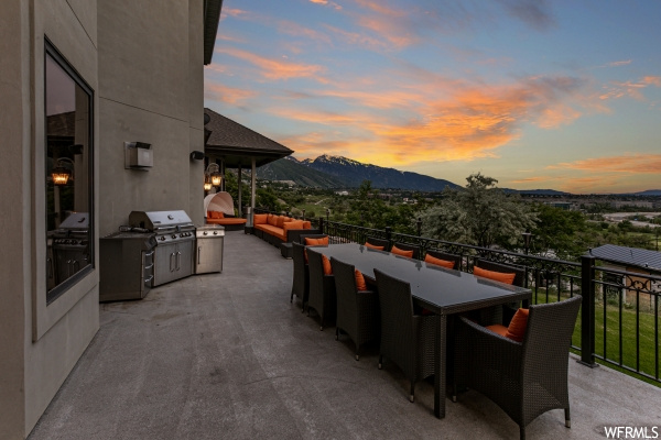 Patio terrace at dusk featuring a balcony, grilling area, and a mountain view
