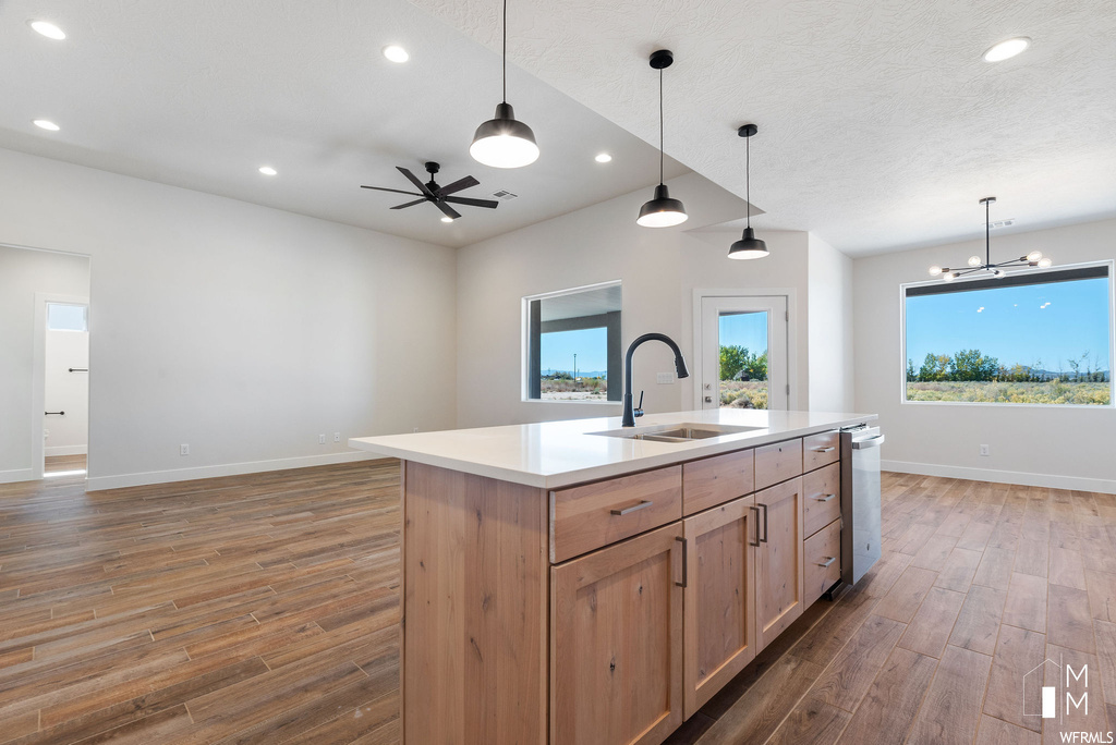 Kitchen with ceiling fan with notable chandelier, an island with sink, dark hardwood / wood-style flooring, and hanging light fixtures
