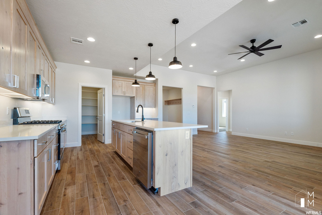Kitchen featuring appliances with stainless steel finishes, light hardwood / wood-style floors, a kitchen island with sink, ceiling fan, and light brown cabinetry
