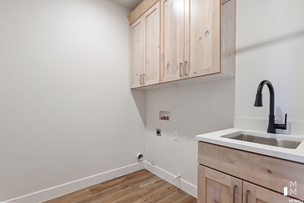 Laundry room featuring light hardwood / wood-style floors, hookup for a gas dryer, sink, cabinets, and electric dryer hookup