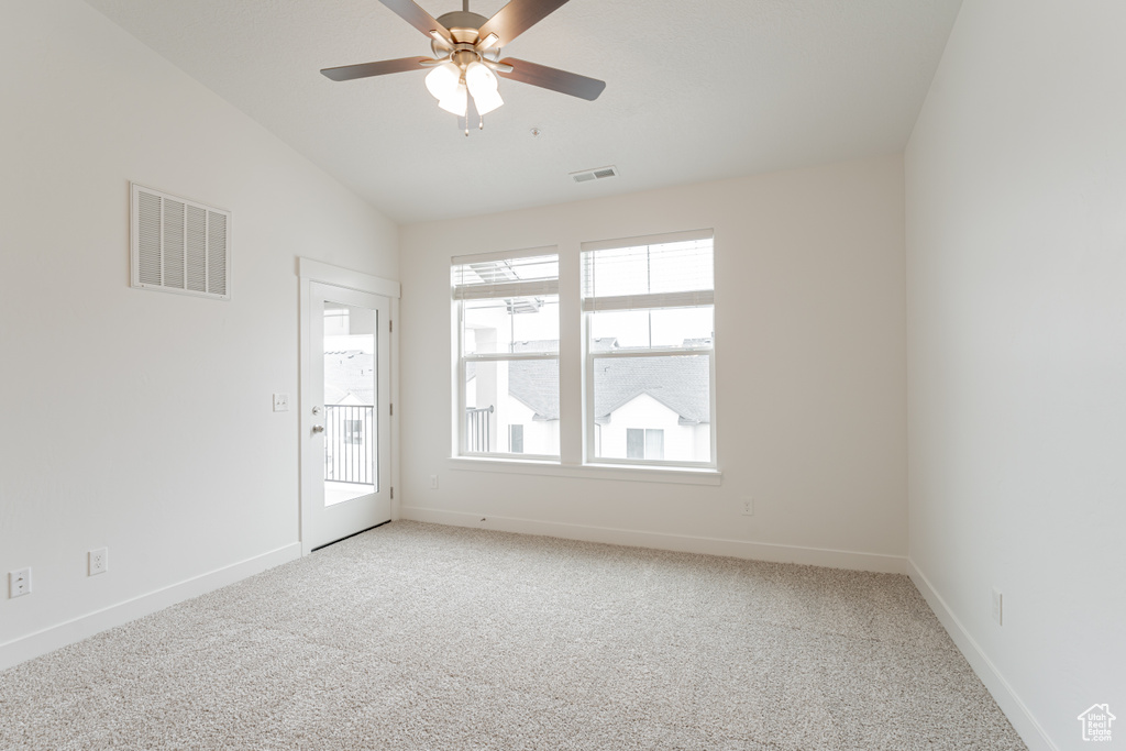 Carpeted empty room with vaulted ceiling, ceiling fan, and a healthy amount of sunlight