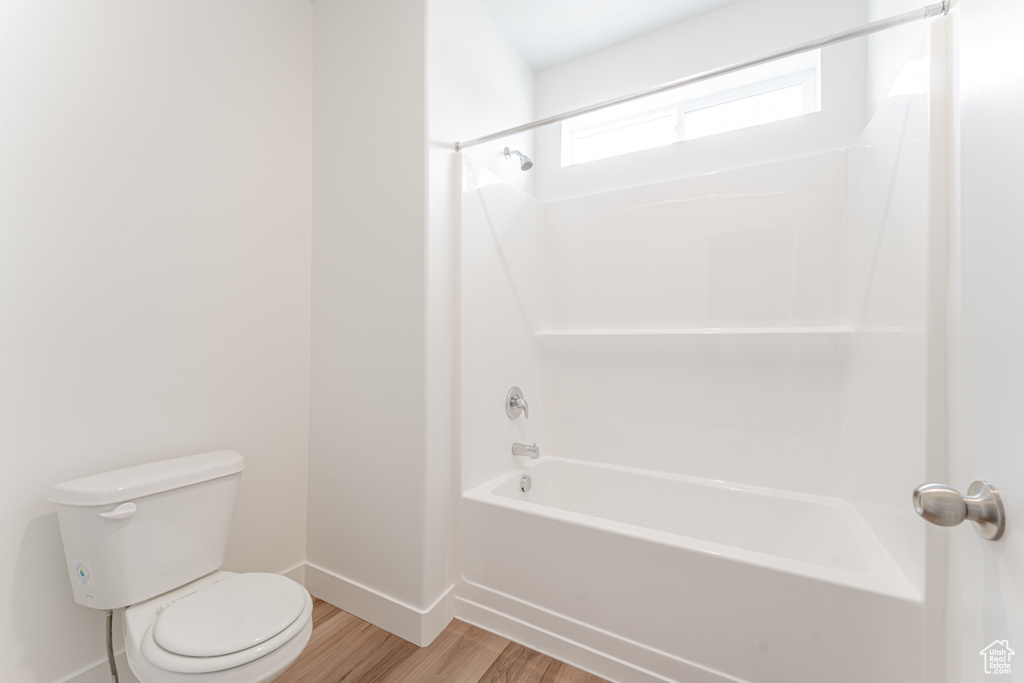 Bathroom with hardwood / wood-style flooring, shower / washtub combination, and toilet