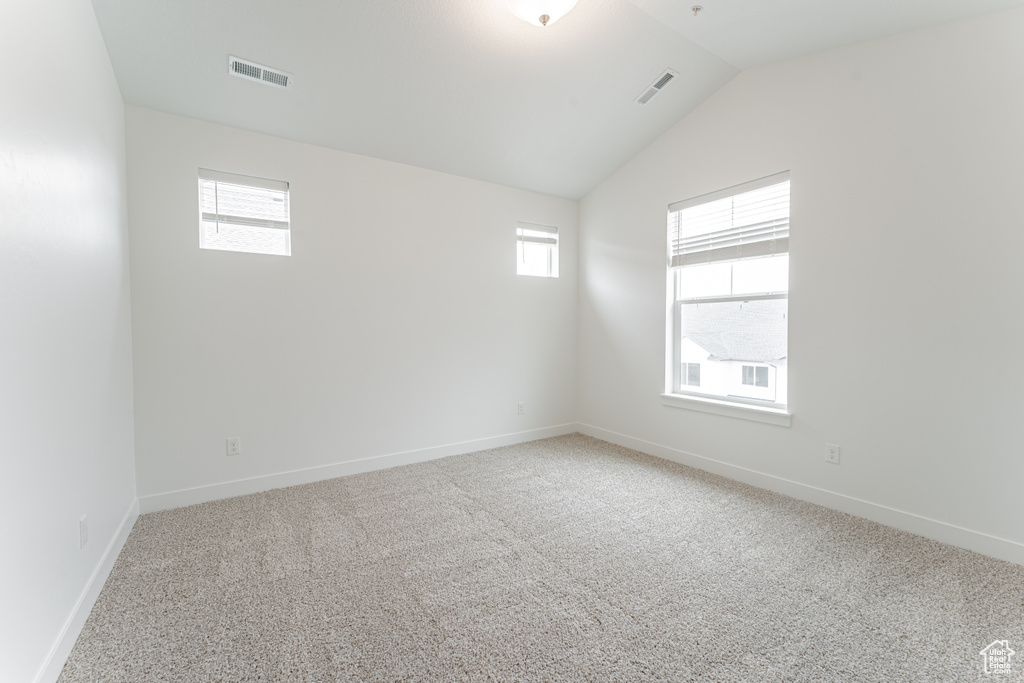 Carpeted empty room with lofted ceiling and a wealth of natural light