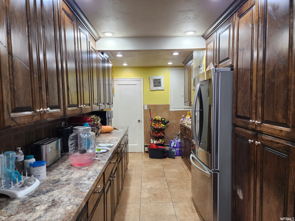 Kitchen featuring light tile flooring, a textured ceiling, backsplash, and stainless steel fridge