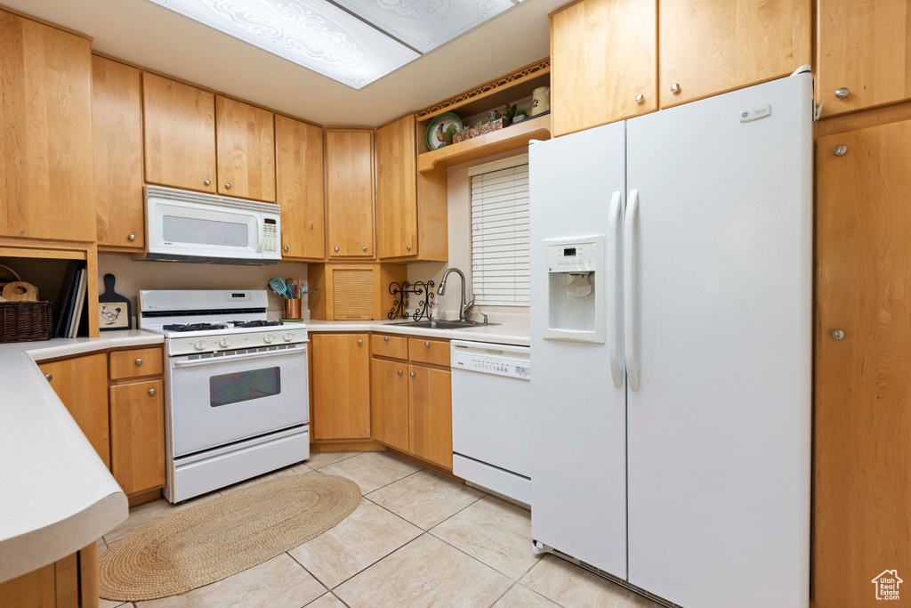 Kitchen featuring sink, white appliances, and light tile floors
