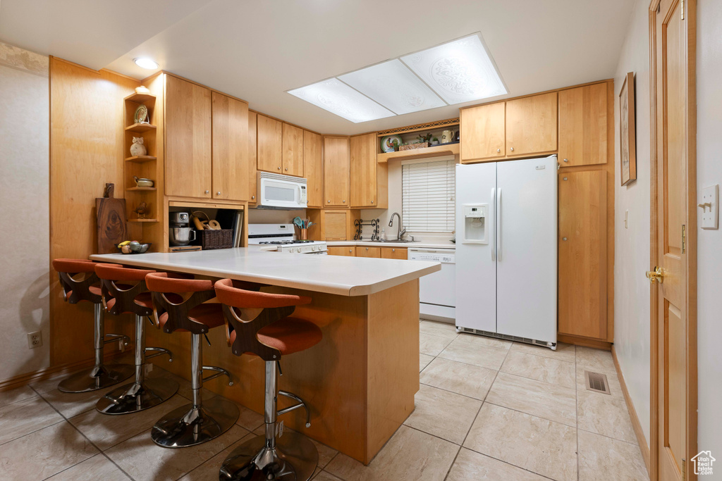 Kitchen with a breakfast bar, white appliances, kitchen peninsula, sink, and light tile floors