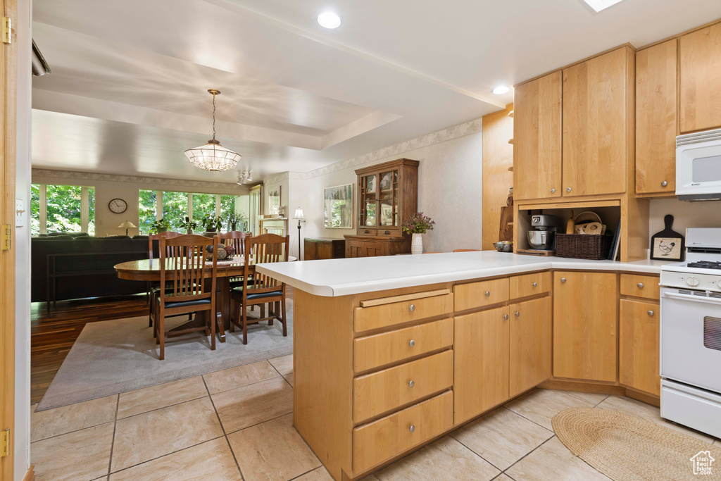 Kitchen with white appliances, kitchen peninsula, light tile floors, and decorative light fixtures