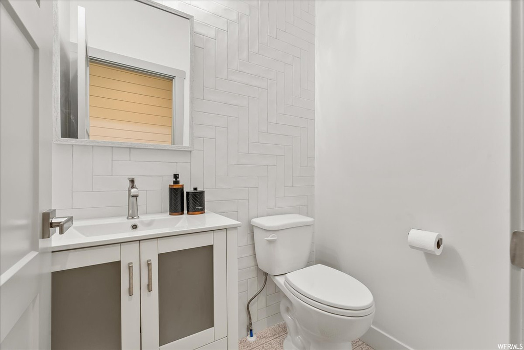 Bathroom with tile floors, large vanity, toilet, and tile walls