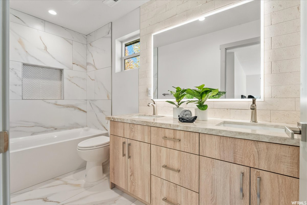 Bathroom with dual vanity, tile floors, toilet, and tile walls
