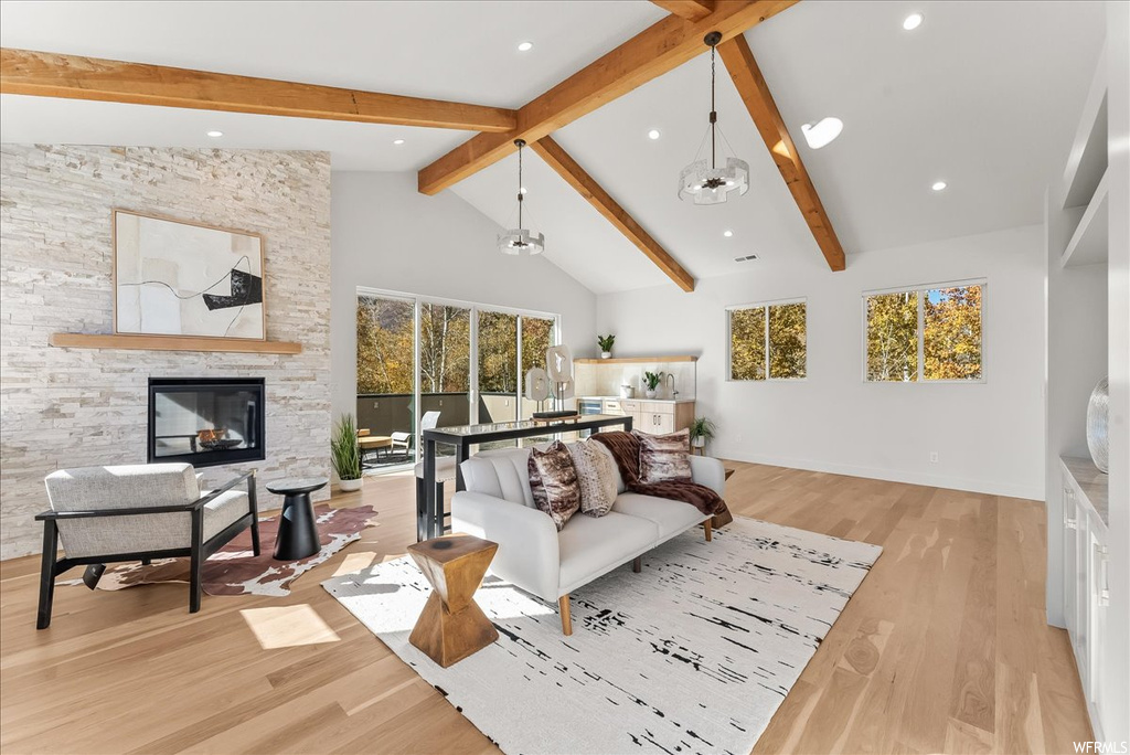 Living room with light hardwood / wood-style flooring, a fireplace, high vaulted ceiling, a notable chandelier, and beamed ceiling
