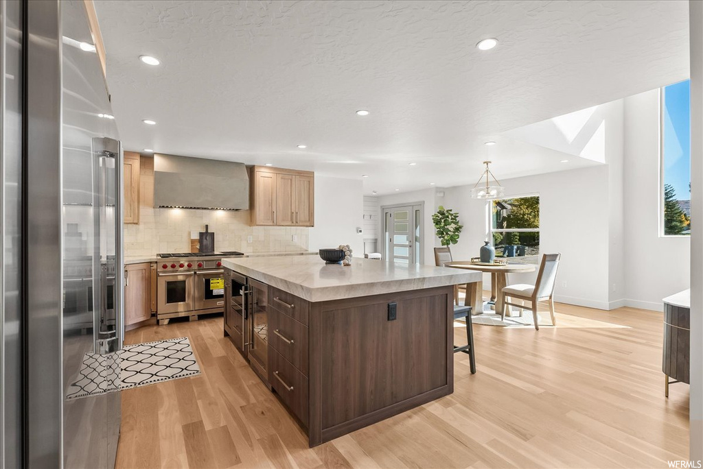 Kitchen featuring light hardwood / wood-style flooring, wall chimney range hood, backsplash, and range with two ovens