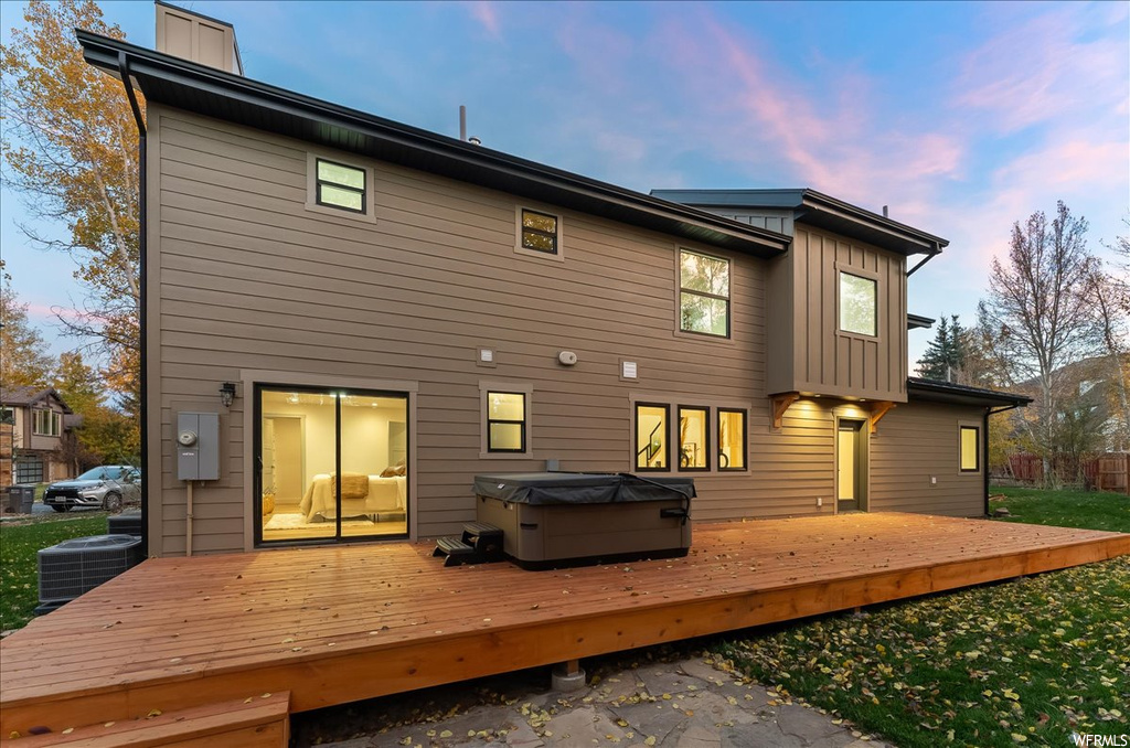 Back house at dusk with a hot tub, a wooden deck, and central AC unit