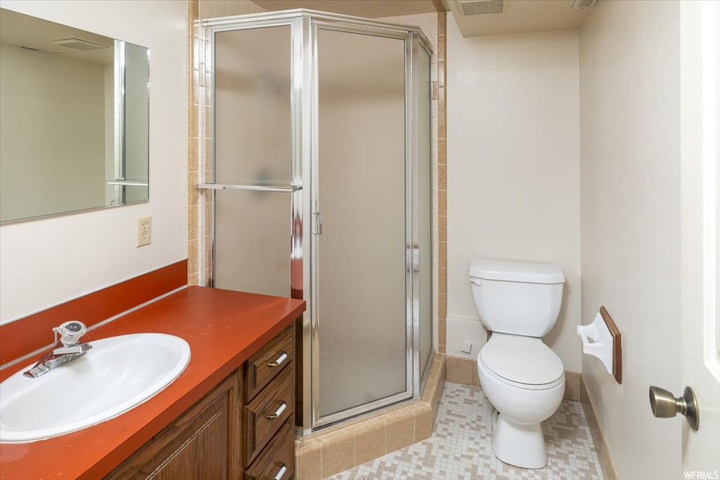 Bathroom featuring tile flooring, a shower with door, vanity, and toilet