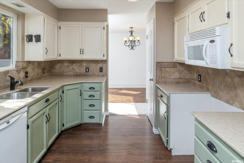 Kitchen featuring dark wood-type flooring, white appliances, backsplash, white cabinets, and a notable chandelier