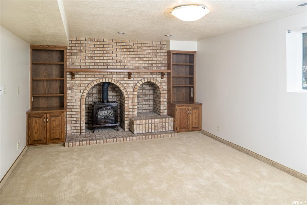 Unfurnished living room with a textured ceiling, a wood stove, brick wall, and light colored carpet