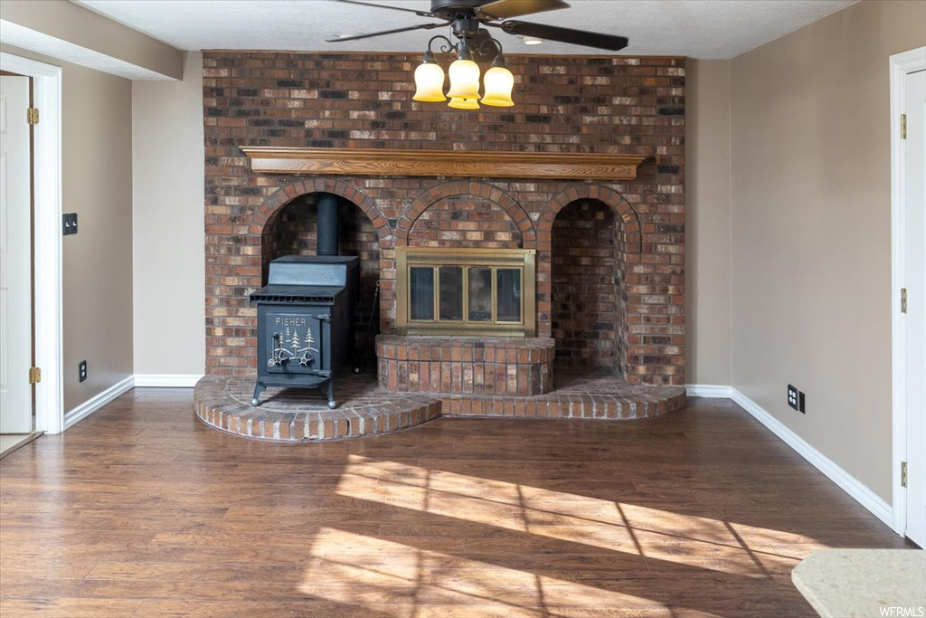 Unfurnished living room with a brick fireplace, a textured ceiling, dark hardwood / wood-style flooring, a wood stove, and ceiling fan
