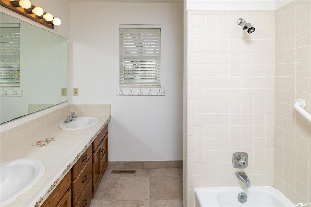 Bathroom with oversized vanity, tiled shower / bath combo, tile flooring, and double sink
