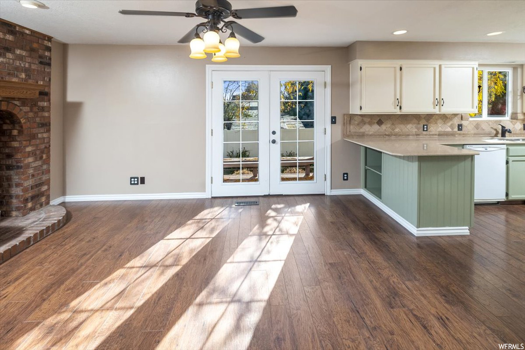 Kitchen featuring brick wall, dark wood-type flooring, tasteful backsplash, white cabinetry, and white dishwasher
