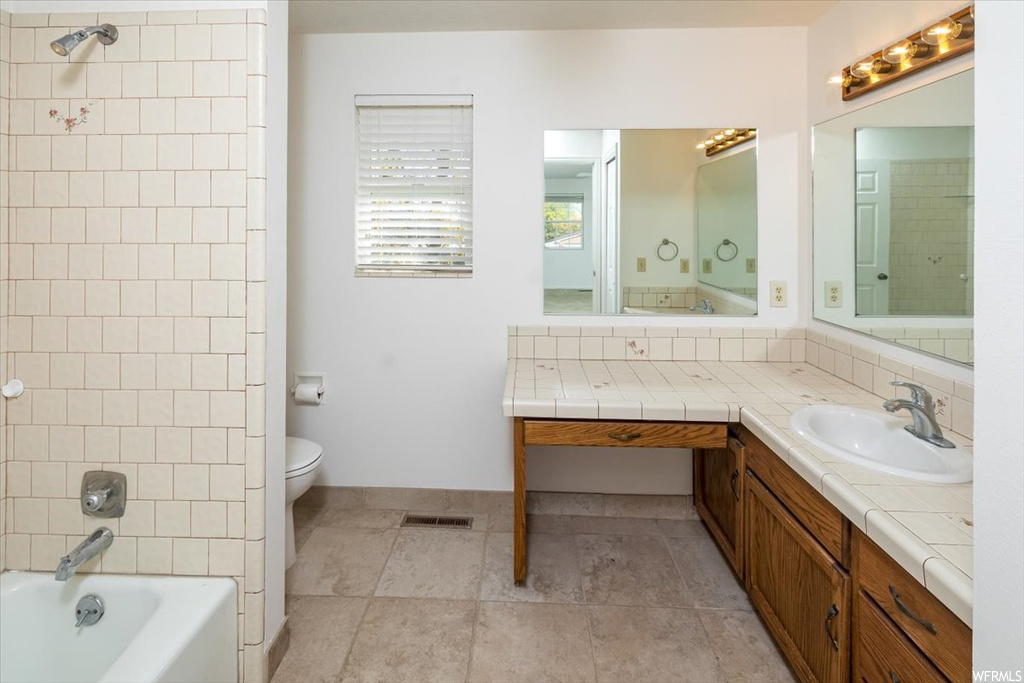 Full bathroom with tile floors, oversized vanity, toilet, and tiled shower / bath