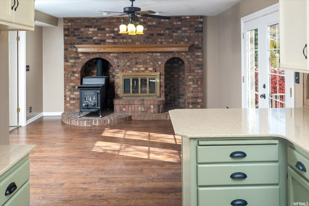 Kitchen with wood-type flooring, green cabinets, a wood stove, french doors, and ceiling fan