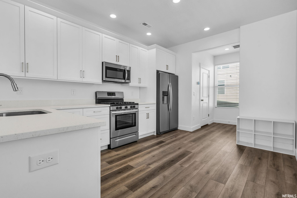 Kitchen featuring sink, white cabinets, dark hardwood flooring, light stone countertops, and appliances with stainless steel finishes