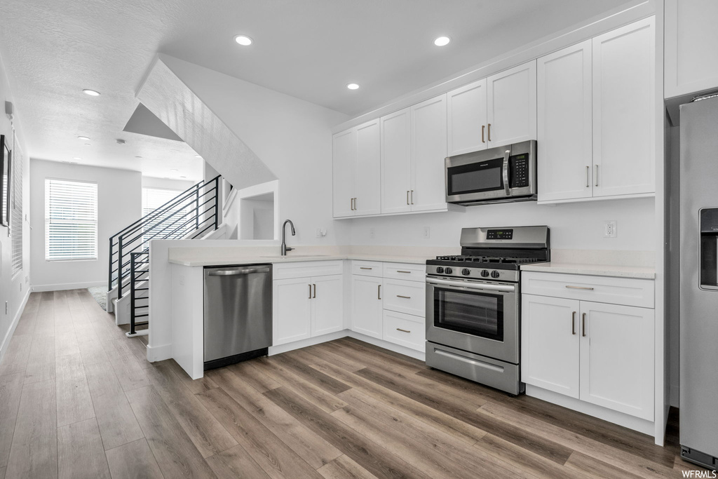 Kitchen with white cabinetry, hardwood flooring, and appliances with stainless steel finishes