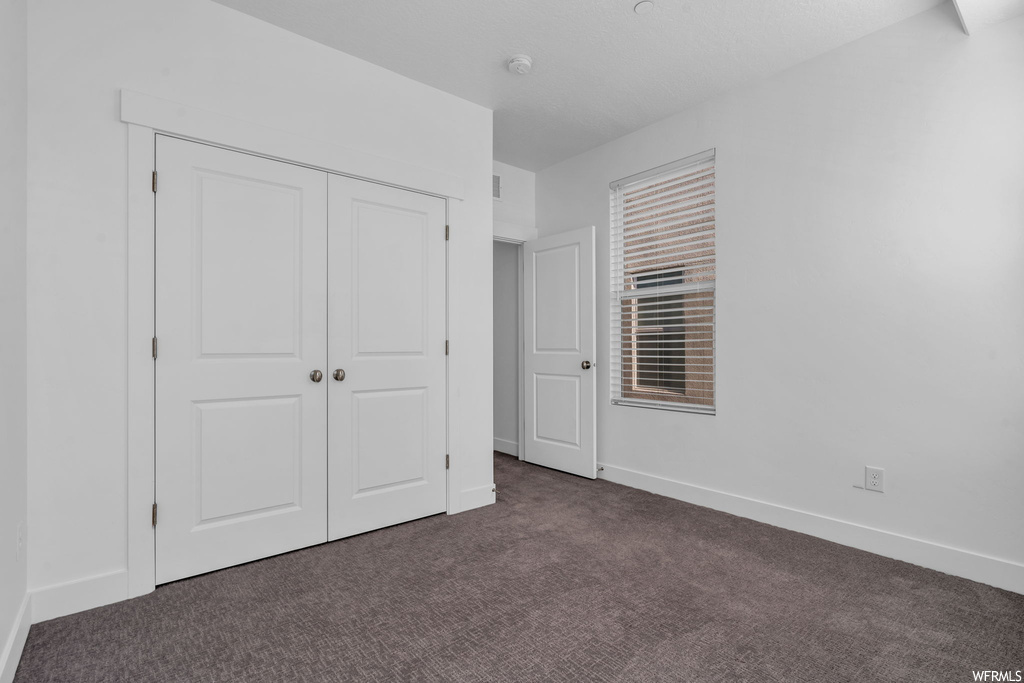 Unfurnished bedroom with dark carpet and a closet