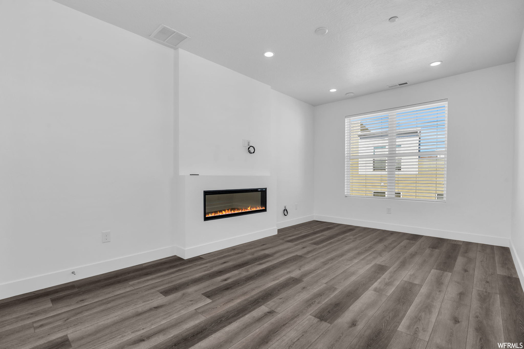 Unfurnished living room featuring dark hardwood flooring and a fireplace