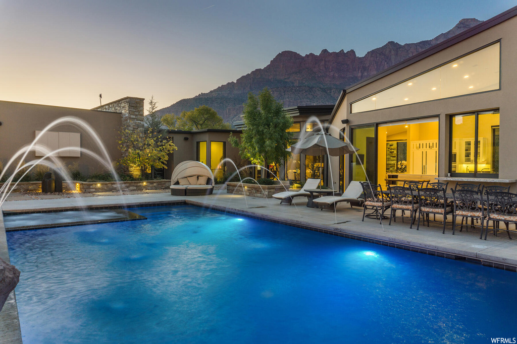 Pool at dusk with a patio area, pool water feature, and a mountain view