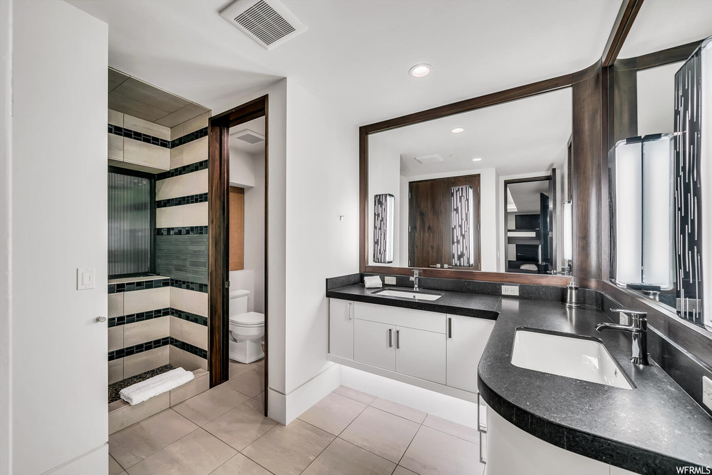 Bathroom featuring dual vanity, toilet, and tile flooring