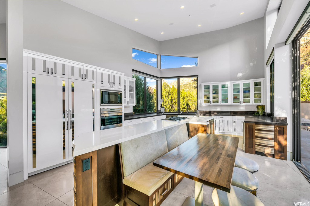Kitchen with light tile floors, appliances with stainless steel finishes, a kitchen island, white cabinets, and a towering ceiling