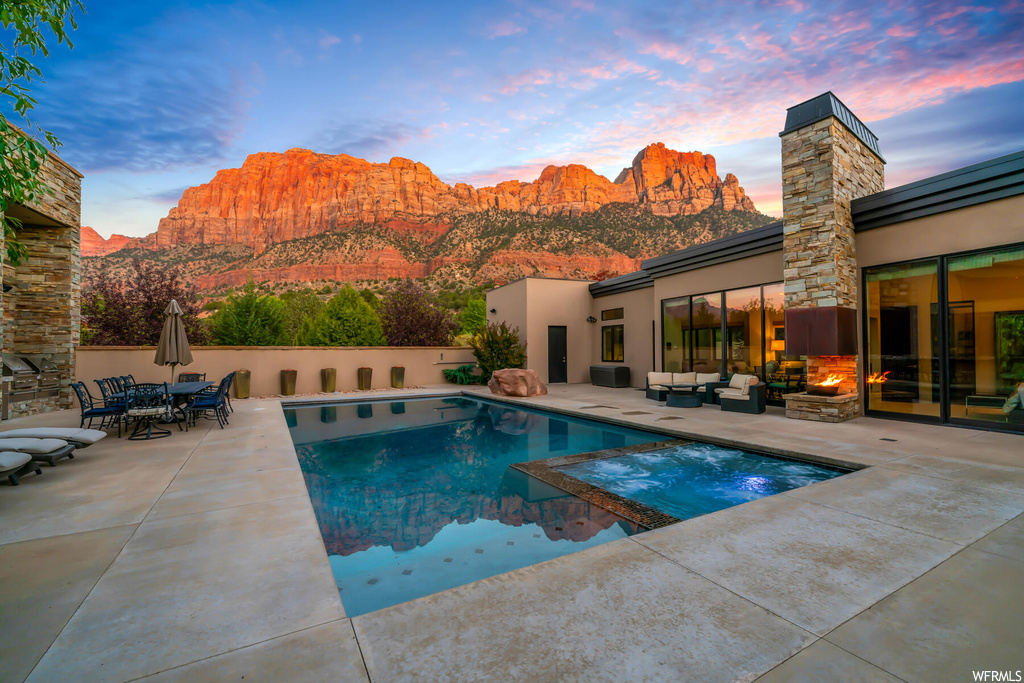 Pool at dusk featuring a mountain view, outdoor lounge area, and a patio