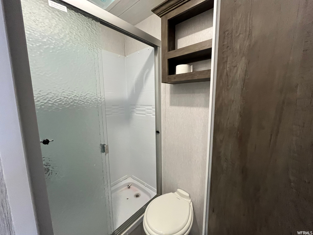 Bathroom featuring a shower with door and toilet