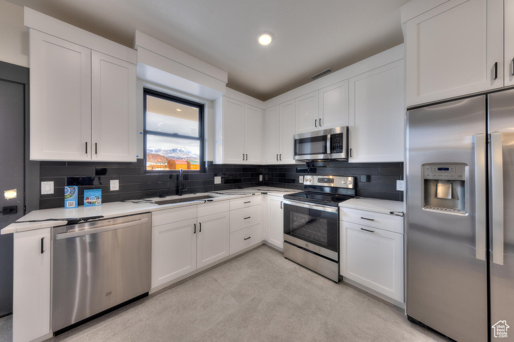 Kitchen featuring white cabinetry, sink, stainless steel appliances, and backsplash