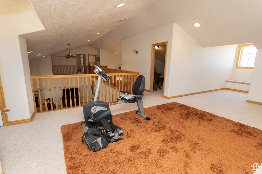 Workout area with a textured ceiling, carpet flooring, ceiling fan, and vaulted ceiling