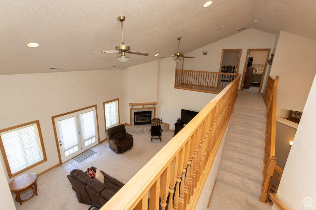 Stairs featuring ceiling fan, a tiled fireplace, light carpet, and high vaulted ceiling