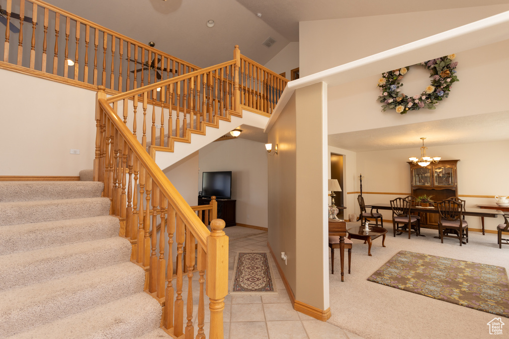 Staircase with high vaulted ceiling, an inviting chandelier, and carpet