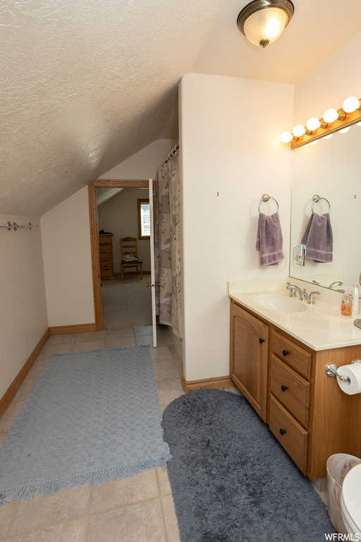 Bathroom featuring toilet, tile floors, large vanity, a textured ceiling, and vaulted ceiling
