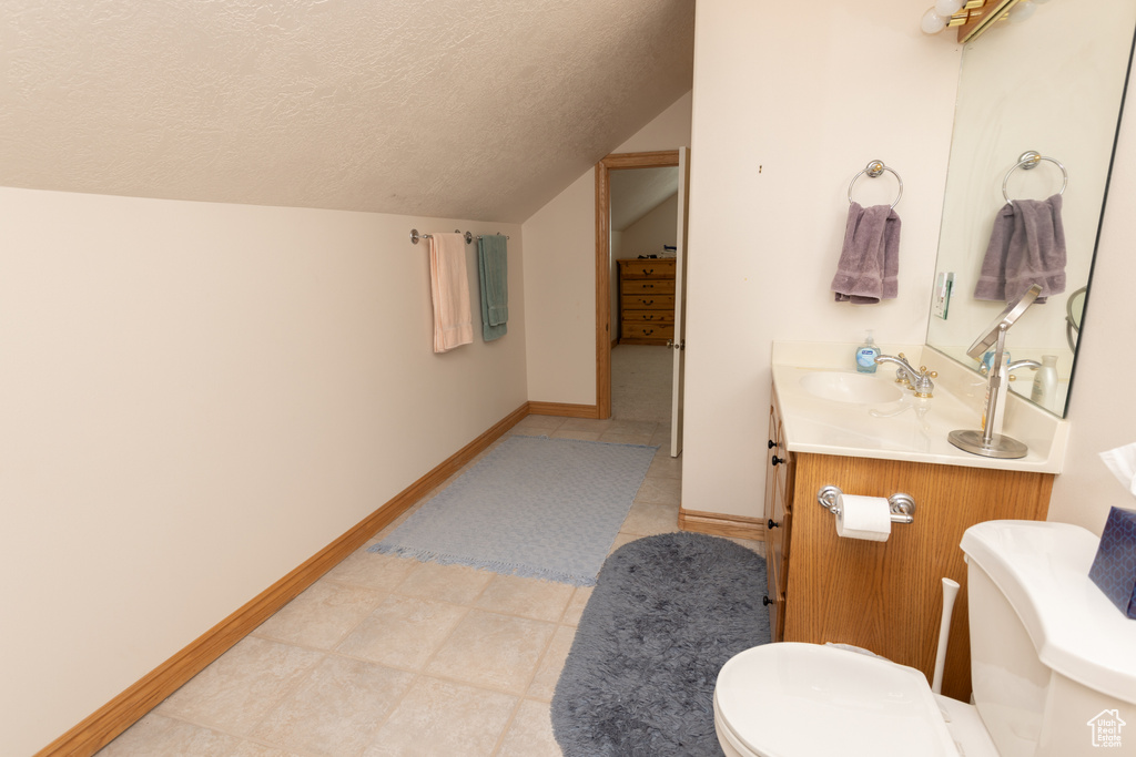 Bathroom featuring a textured ceiling, lofted ceiling, tile floors, vanity, and toilet