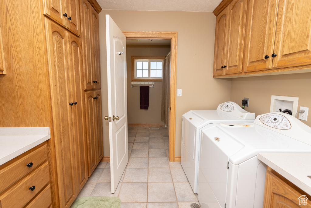 Clothes washing area with washer and dryer, cabinets, hookup for a washing machine, electric dryer hookup, and light tile floors