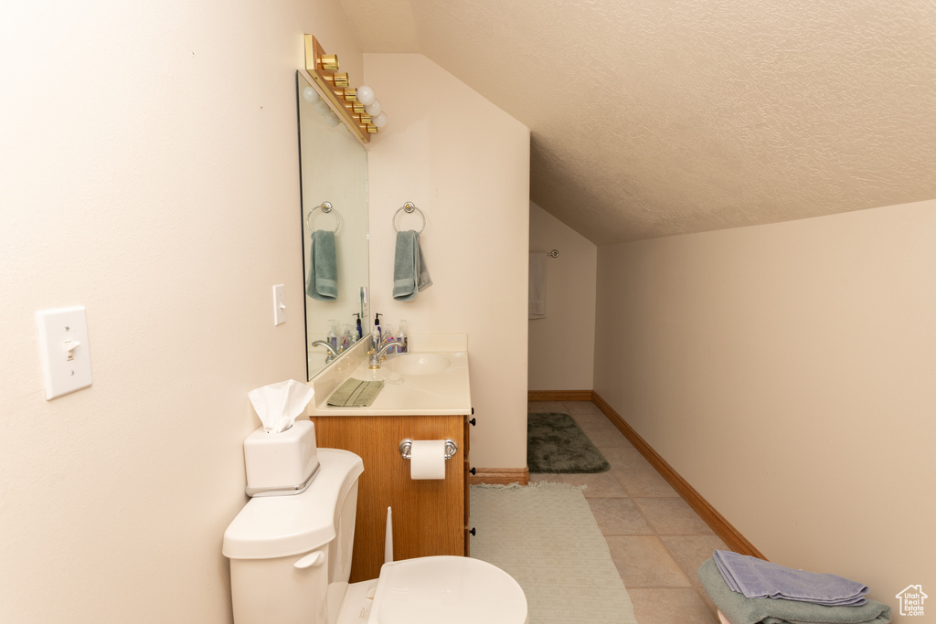 Bathroom with toilet, tile flooring, vanity, a textured ceiling, and lofted ceiling