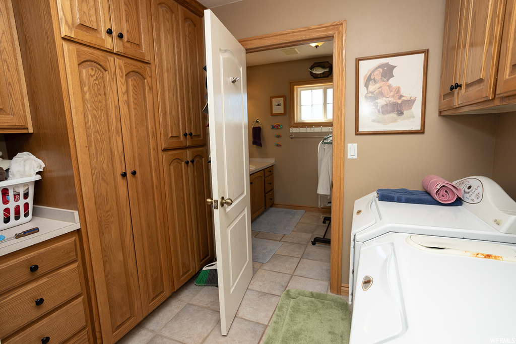 Laundry area with washer and dryer, light tile floors, and cabinets