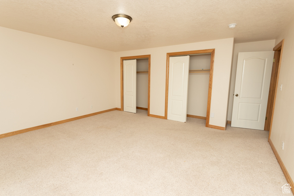 Unfurnished bedroom featuring carpet, a textured ceiling, and multiple closets