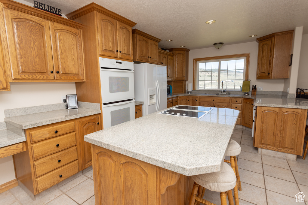 Kitchen featuring a kitchen island, a kitchen breakfast bar, white appliances, and light tile floors