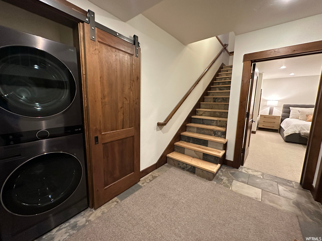 Laundry area featuring a barn door, stacked washing maching and dryer, and light colored carpet