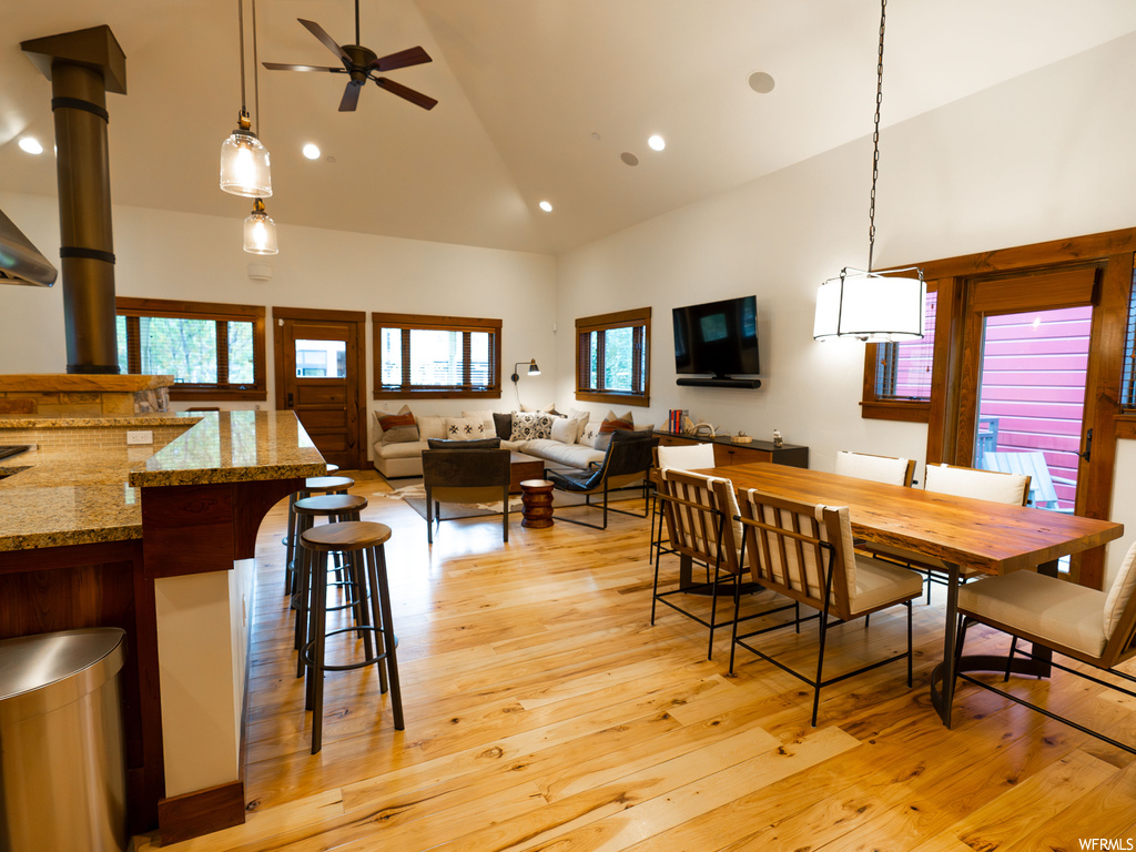 Dining area with light wood-type flooring, a wood stove, high vaulted ceiling, and ceiling fan