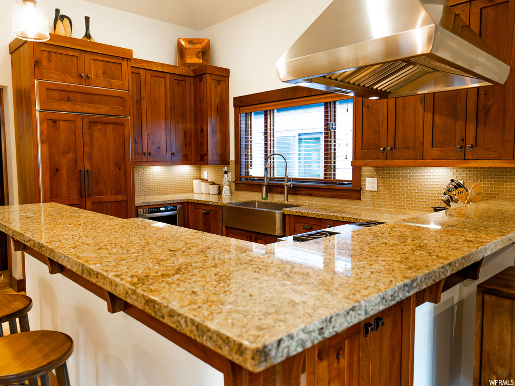 Kitchen featuring sink, ventilation hood, tasteful backsplash, a kitchen breakfast bar, and paneled built in fridge