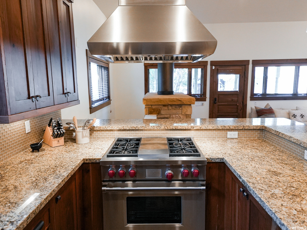 Kitchen featuring backsplash, island exhaust hood, designer stove, and light stone countertops