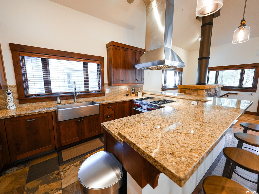 Kitchen featuring sink, backsplash, island exhaust hood, gas stove, and light stone counters