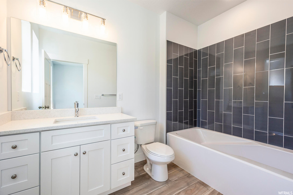 Full bathroom featuring hardwood / wood-style floors, toilet, vanity, and tiled shower / bath combo